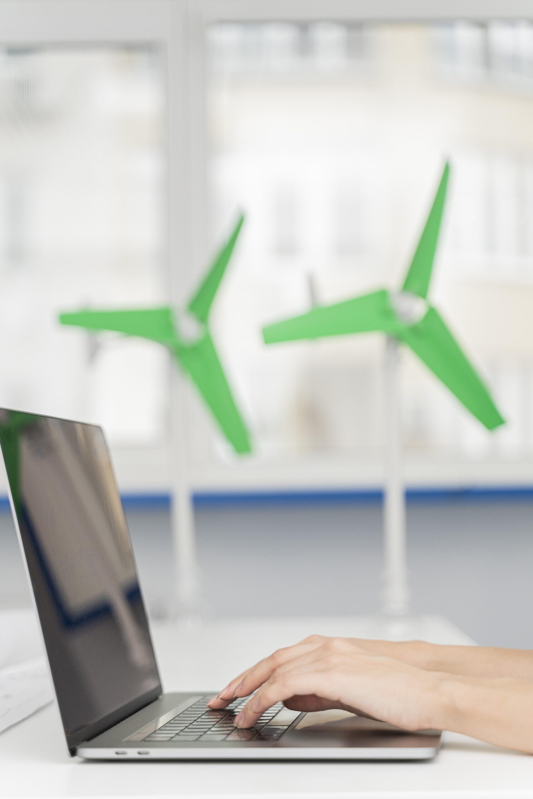 Dłonie ludzkie piszące na laptopie z makietami wiatraków w tle